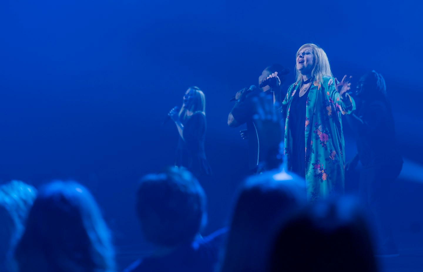 Een vrouw in een bloemenjasje zingt in een microfoon.