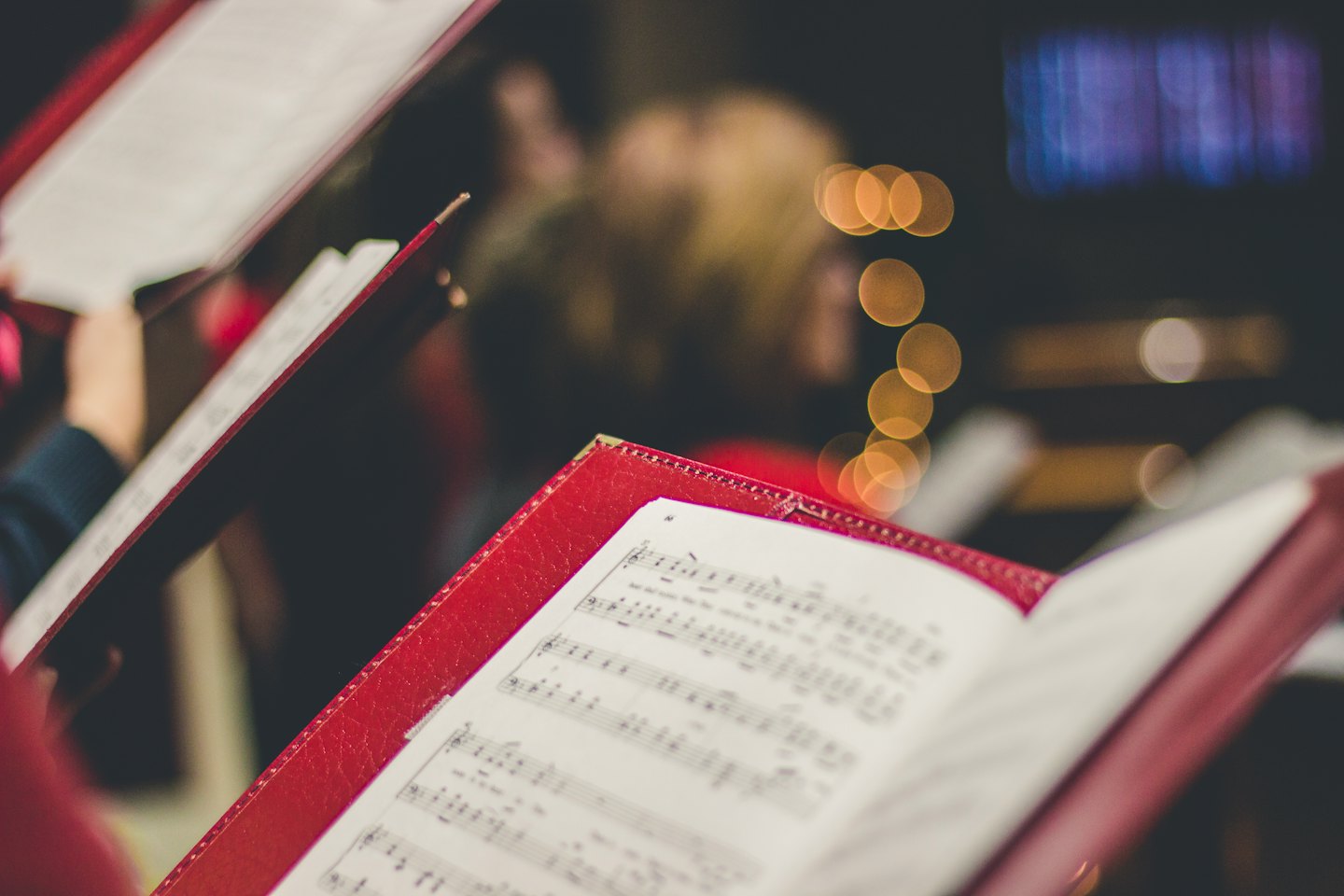 Handen die open rode ordners met bladmuziek vasthouden.