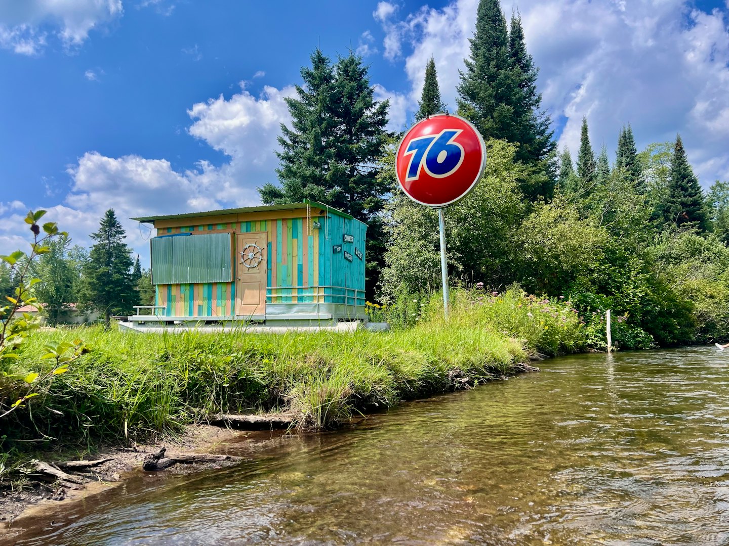 Kleurrijk rustiek huisje met een rood bord aan de rivier.