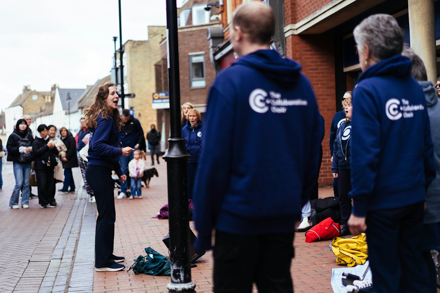 Koorleden in marineblauwe hoodies die op een straat van baksteen zingen.