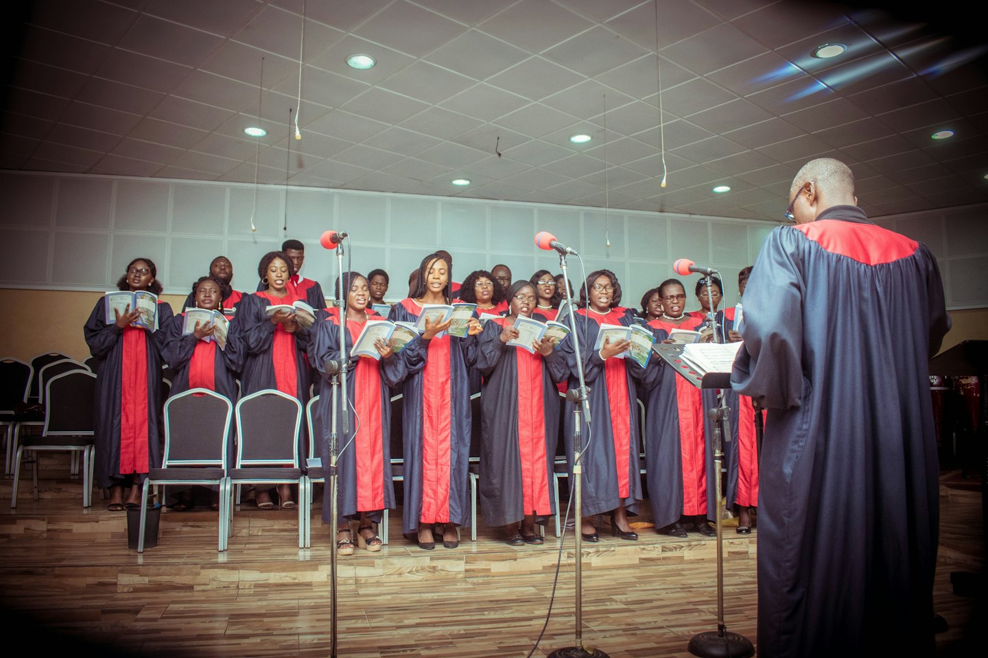 Een koor in gewaden zingt samen uit liedboeken op een houten podium.